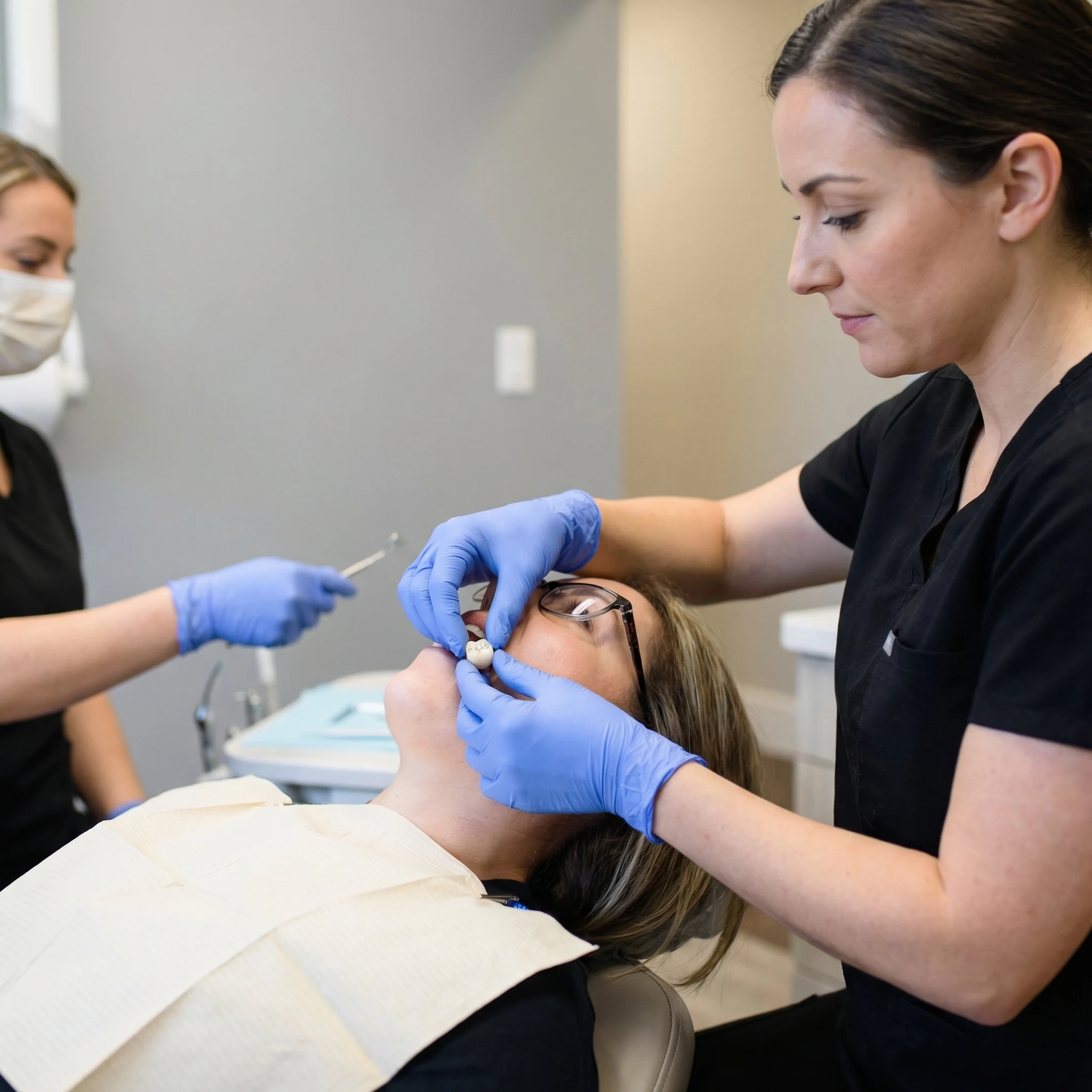 Dentist in black scrubs with latex gloves placing dental crown on patient's tooth during procedure Dalton GA